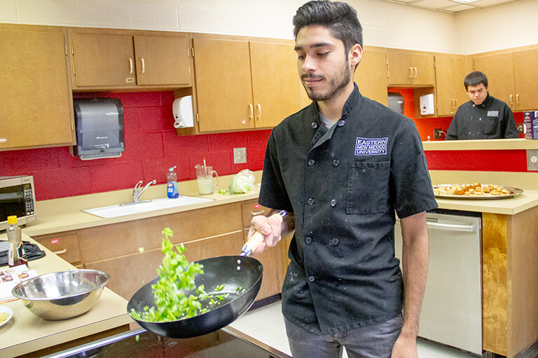 Culinary Arts student flips food in a pan over a stove