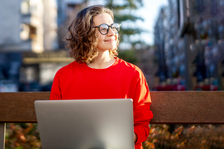 woman on bench looks up from computer smiling