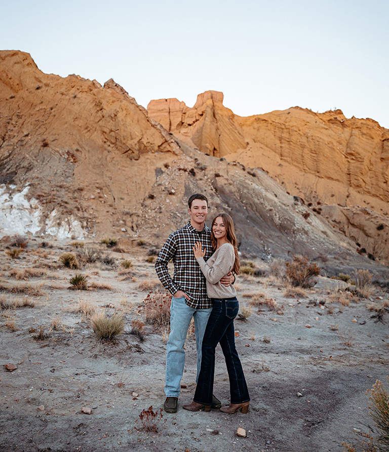 Marissa McCulloch and her fianc&eacute; stand together in front of sandstone cliffs.